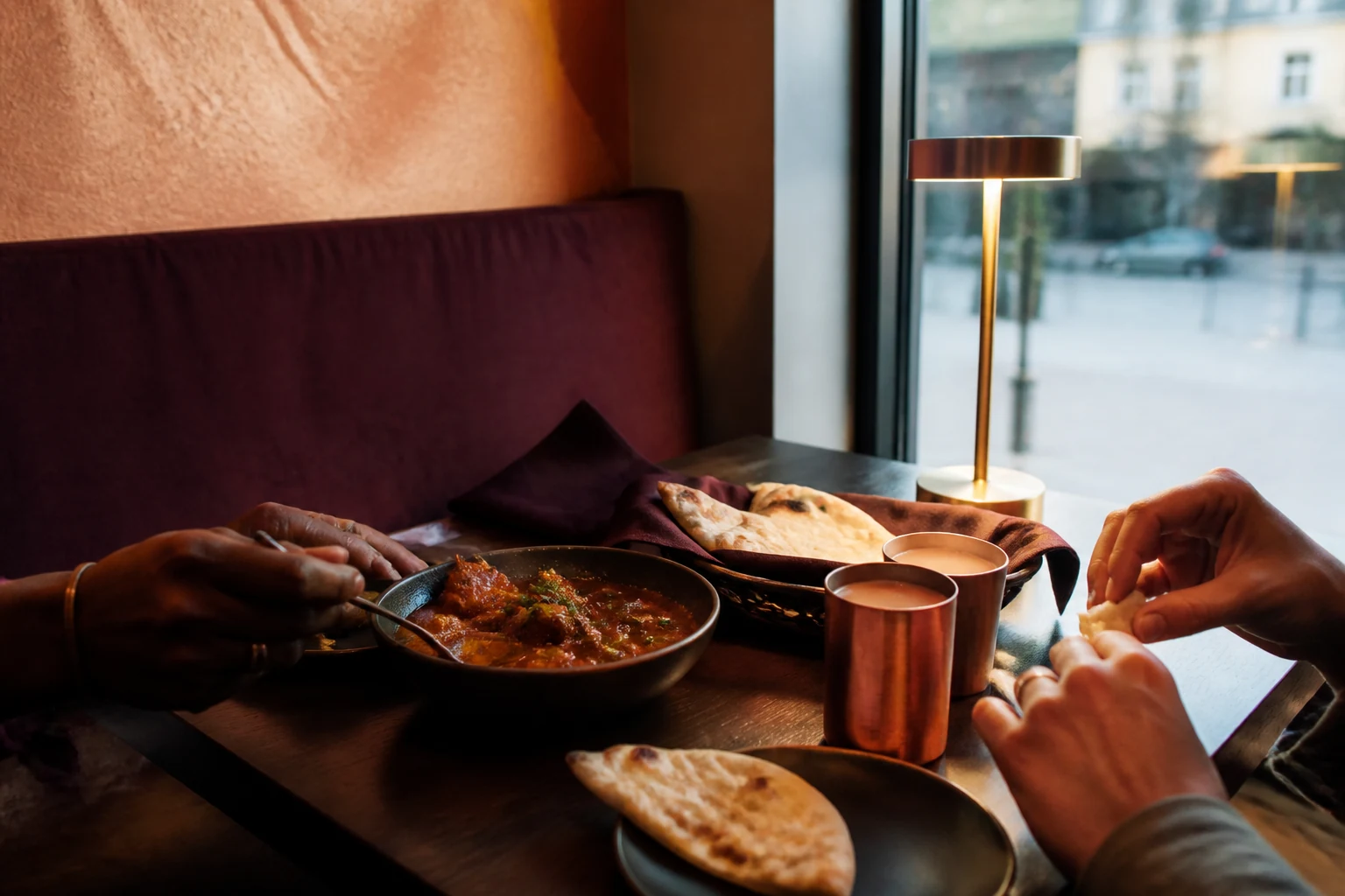 Two diners sharing Indian food and chai beside a window