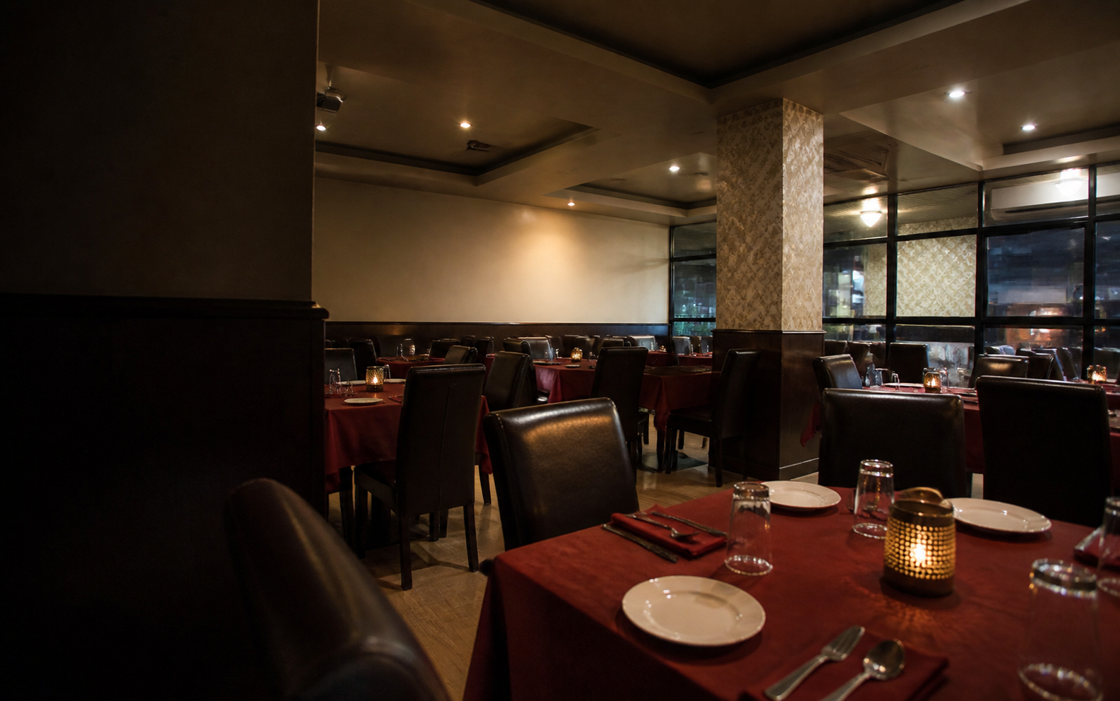 Warm restaurant dining room with red table linens and dark chairs